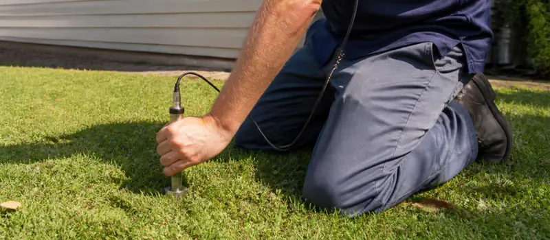 Technician kneeling on a lawn pressing a leak detection probe into the grass